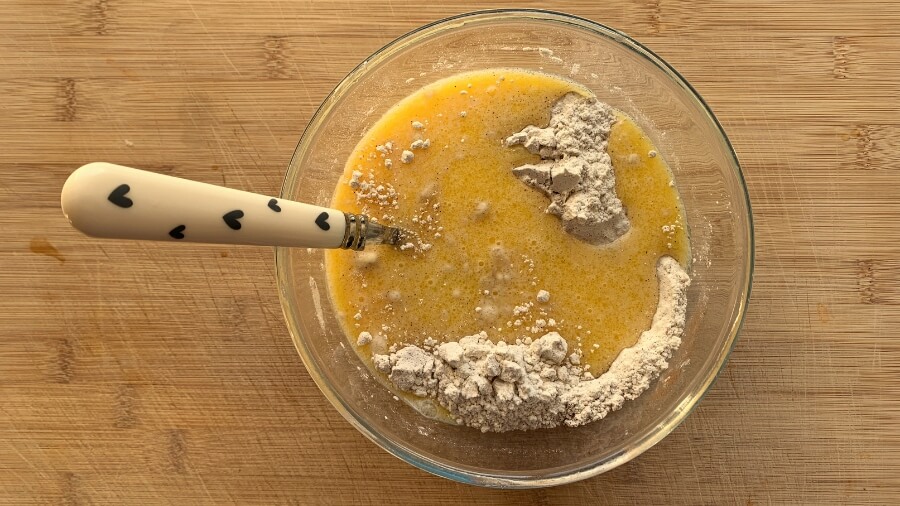 The process of making homemade donut hole dough, showing a mix of wet and dry ingredients in a large glass bowl with a heart-patterned spatula.