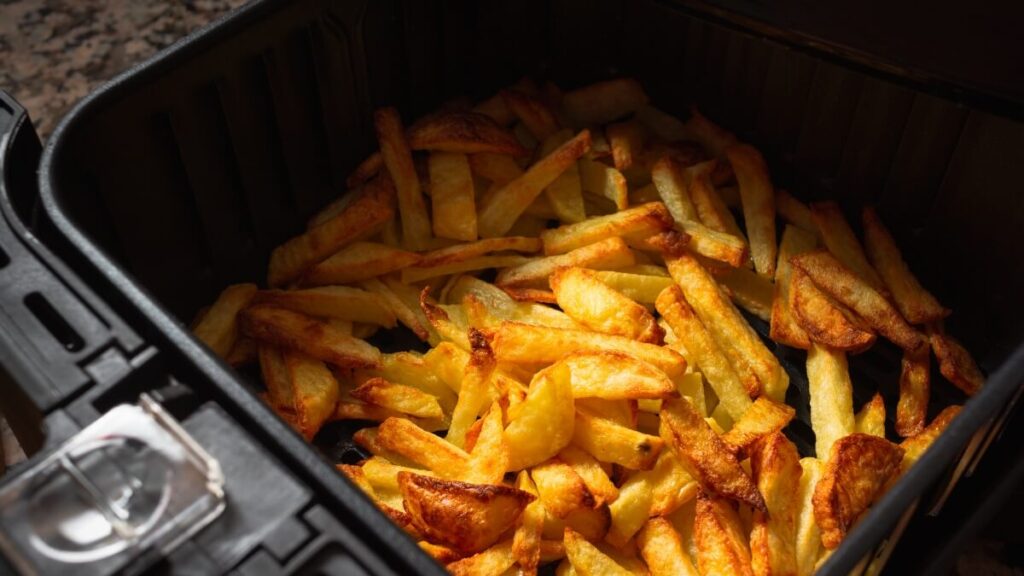 A basket of golden-brown French fries freshly cooked in an air fryer, with visible crisp edges and soft centers, sitting in a black basket with a handle.


